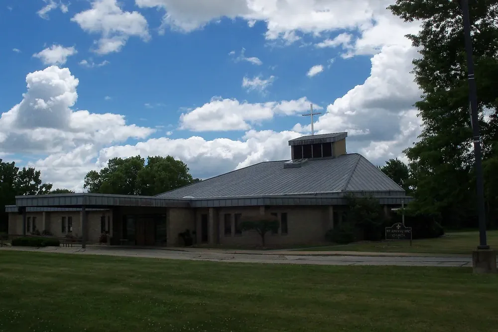 Saint Joan of Arc Church on a wide lawn under summer clouds in Streetsboro, Ohio